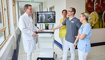 Dr. med. Ansgar Platte und drei Mitarbeitende stehen um einen mobilen Monitor und betrachten gemeinsam Röntgenbilder.