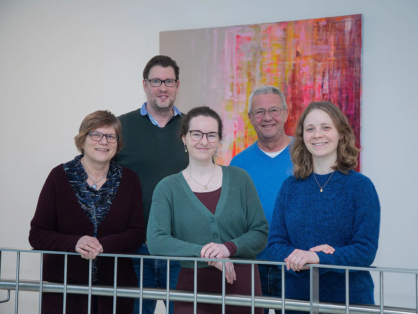 Fünf Menschen stehen vor einem Bild und lächeln in die Kamera.