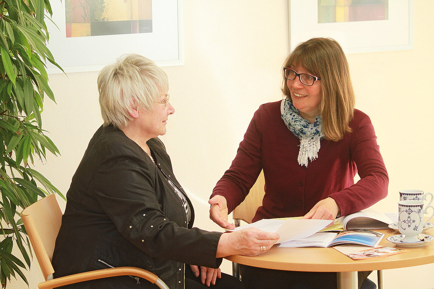 Zwei Frauen sitzen an einem Tisch und besprechen gemeinsam Unterlagen und Informationsmaterial.