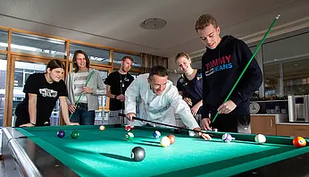 Kinder und Jugendliche spielen gemeinsam Billard, begleitet von einem ärztlichen Mitarbeiter in weißem Kittel.