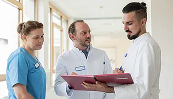 PD Dr. med. Peter Korsten sitzt mit mehreren ärztlichen Kolleginnen an einem Tisch und nimmt an einer Besprechung teil.