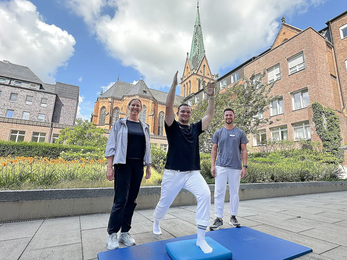 Drei Therapeut:innen machen eine Übung im Stehen auf einer Sportmatte.