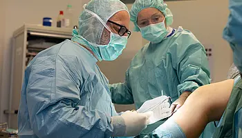 Zwei Mitarbeitende der Klinik für Ambulante Operationen & Sporttraumatologie führen einen ambulanten chirurgischen Eingriff an einem Knie durch.