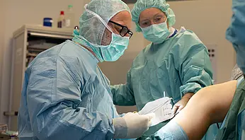 Zwei Mitarbeitende der Klinik für Ambulante Operationen & Sporttraumatologie führen einen ambulanten chirurgischen Eingriff an einem Knie durch.