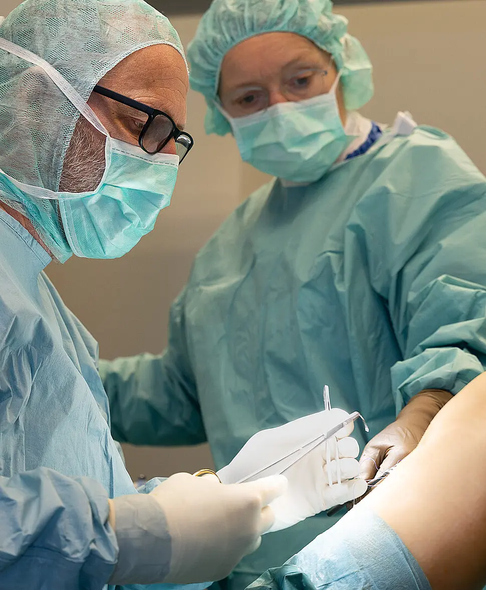 Zwei Mitarbeitende der Klinik für Ambulante Operationen & Sporttraumatologie führen einen ambulanten chirurgischen Eingriff an einem Knie durch.