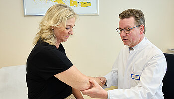 Dr. med. Ansgar Platte überprüft die Beweglichkeit des Ellenbogens einer Patientin, indem er den Arm mit beiden Händen führt.
