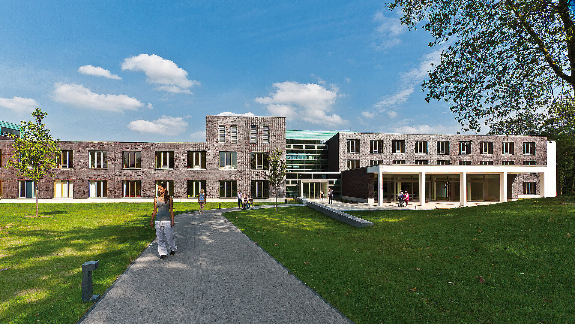 Außenansicht des Reha-Zentrums des St. Josef-Stifts mit begrüntem Gelände und Gehweg, auf dem Menschen unterwegs sind.