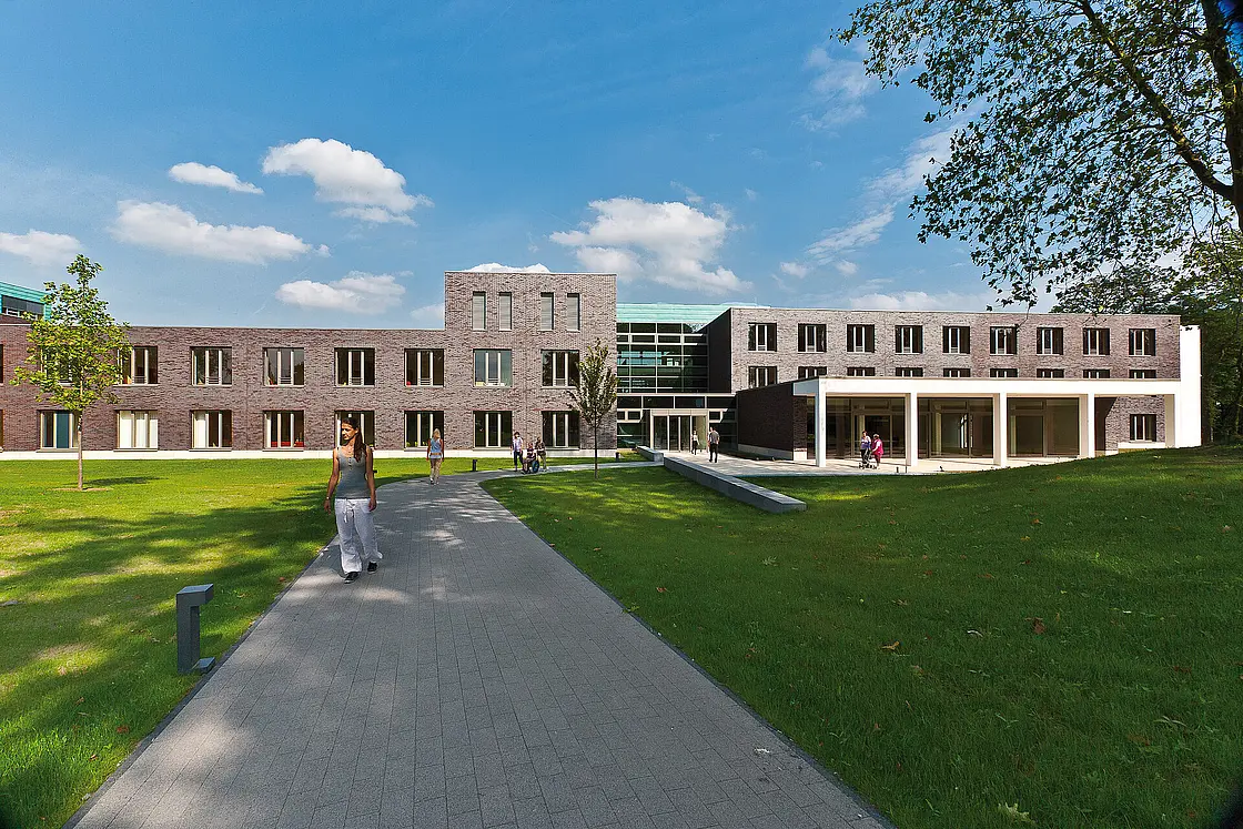 Außenansicht des Reha-Zentrums des St. Josef-Stifts mit begrüntem Gelände und Gehweg, auf dem Menschen unterwegs sind.