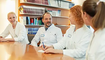 PD Dr. med. Peter Korsten steht einer ärztlichen Kollegin in einem Büro mit Bücherregalen gegenüber.