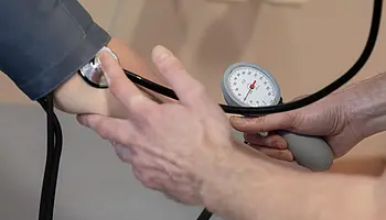 Ein Pfleger misst mit einem manuellen Blutdruckmessgerät den Blutdruck einer Patientin am Arm.