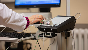 Medizinisches Messgerät mit angeschlossenen Kabeln auf einem Arbeitsplatz während einer Untersuchung.