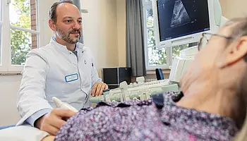 PD Dr. med. Peter Korsten führt mit einem Ultraschallgerät eine Untersuchung an der Hand einer Patientin durch.