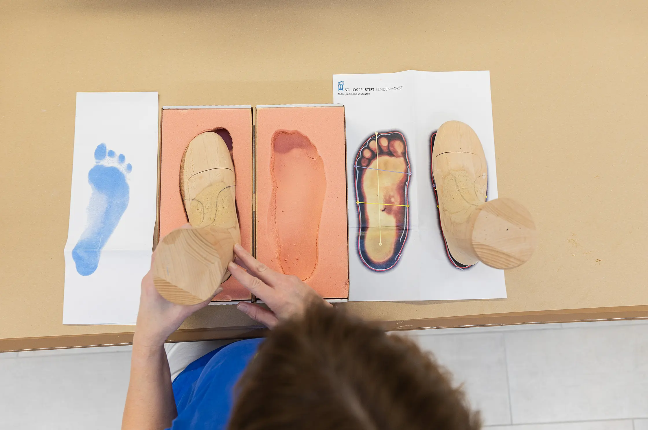 Draufsicht auf Fußabdrucke, Holzleisten und Schablonen, angeordnet auf einem Arbeitstisch zur Vorbereitung der Schuhanfertigung.