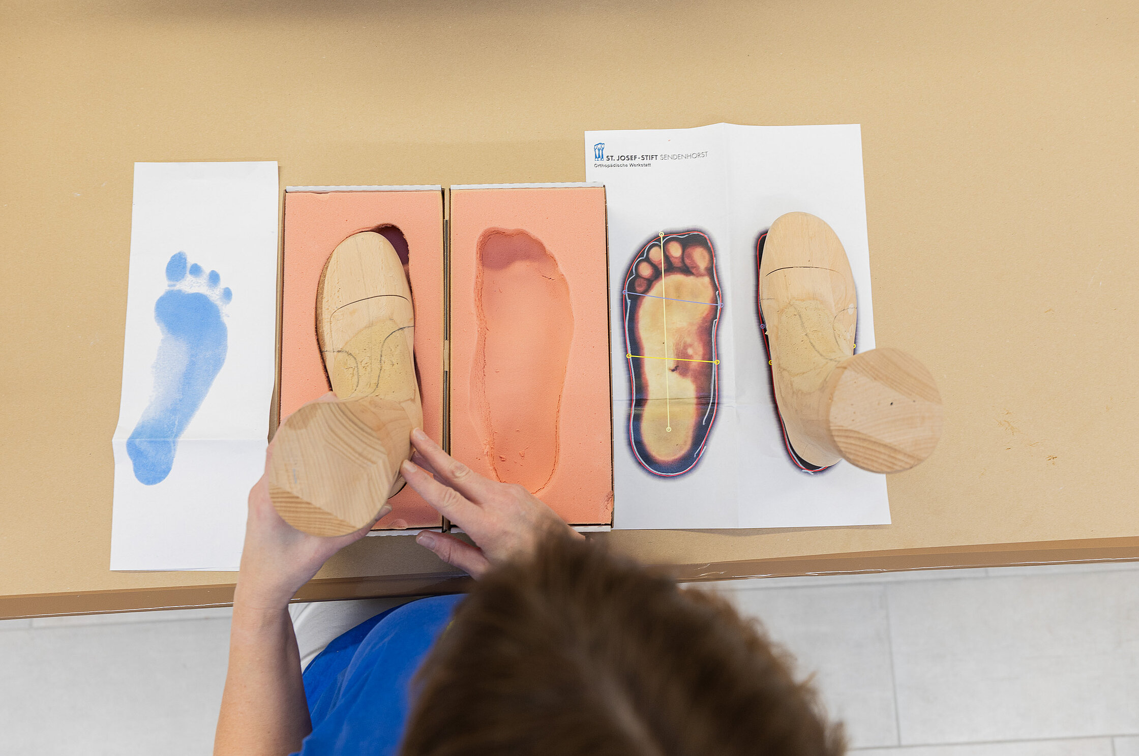 Draufsicht auf Fußabdrucke, Holzleisten und Schablonen, angeordnet auf einem Arbeitstisch zur Vorbereitung der Schuhanfertigung.