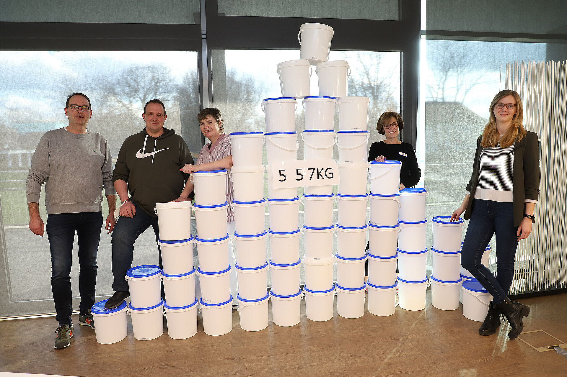 Mitarbeitende stehen neben gestapelten Mehrwegbehältern; ein Schild weist auf die gesammelte Menge eingesparter Verpackung hin.