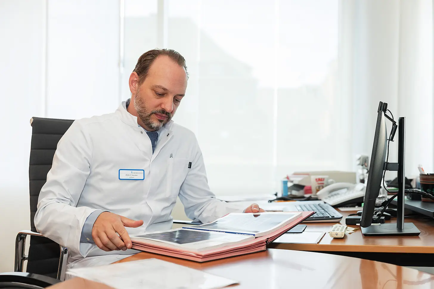 Chefarzt PD Dr. med. Peter Korsten sitzt an seinem Schreibtisch und sichtet medizinische Unterlagen in der rheumatologischen Klinik.