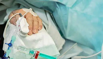 Nahaufnahme einer Patientenhand mit venösem Zugang, Infusionsleitung und angeschlossener Spritze.