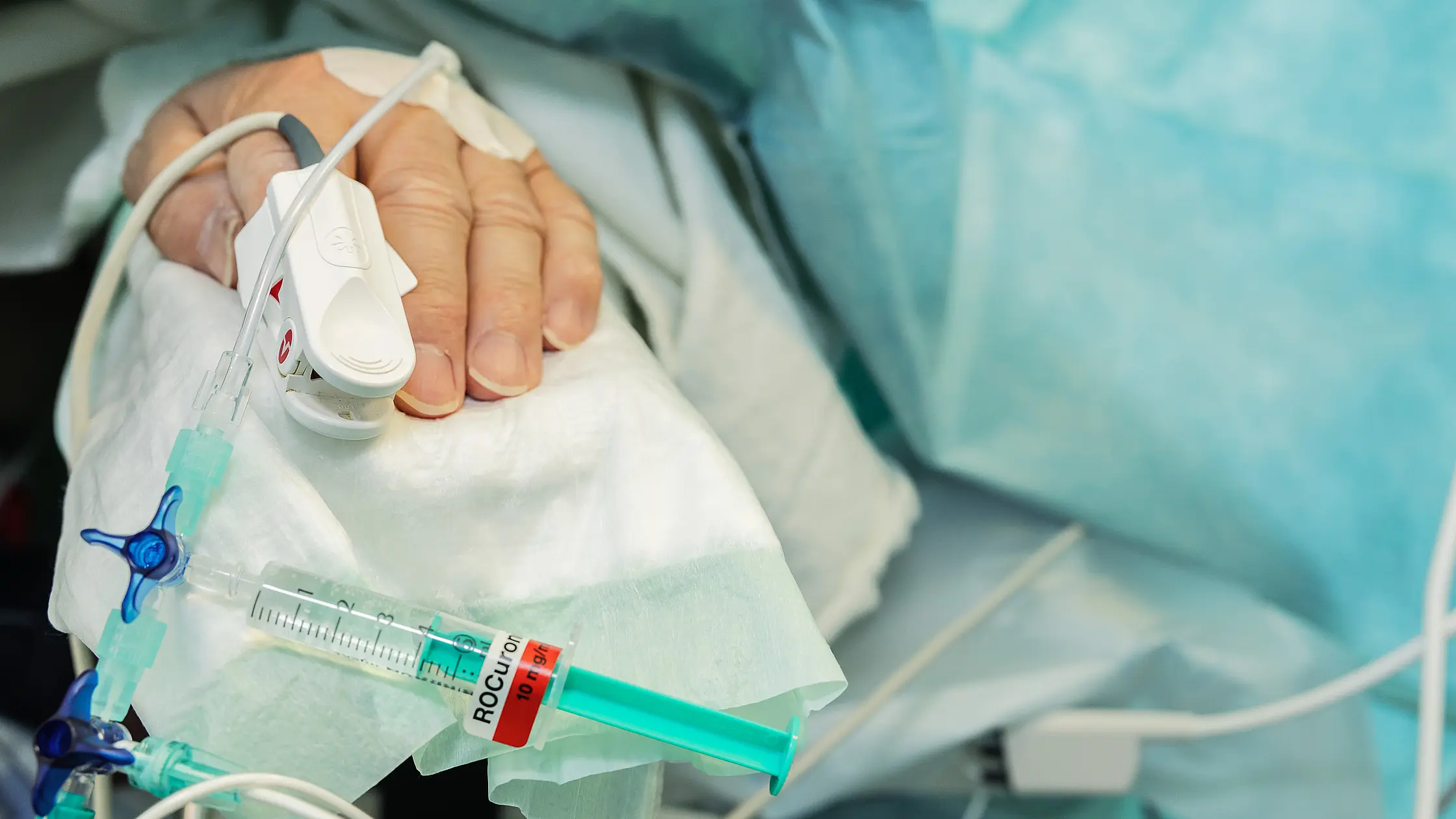 Nahaufnahme einer Patientenhand mit venösem Zugang, Infusionsleitung und angeschlossener Spritze.
