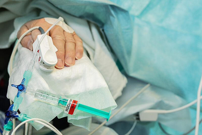 Nahaufnahme einer Patientenhand mit venösem Zugang, Infusionsleitung und angeschlossener Spritze.