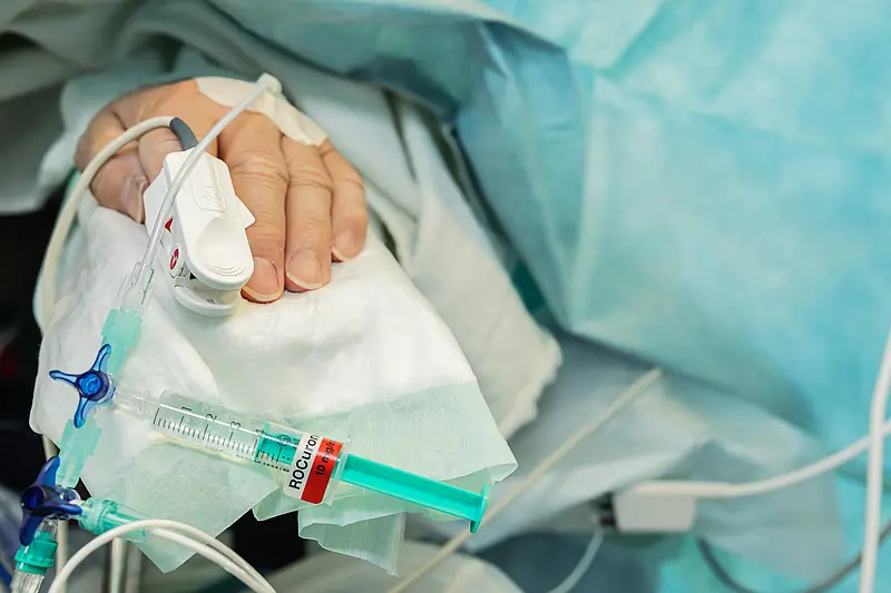 Nahaufnahme einer Patientenhand mit venösem Zugang, Infusionsleitung und angeschlossener Spritze.