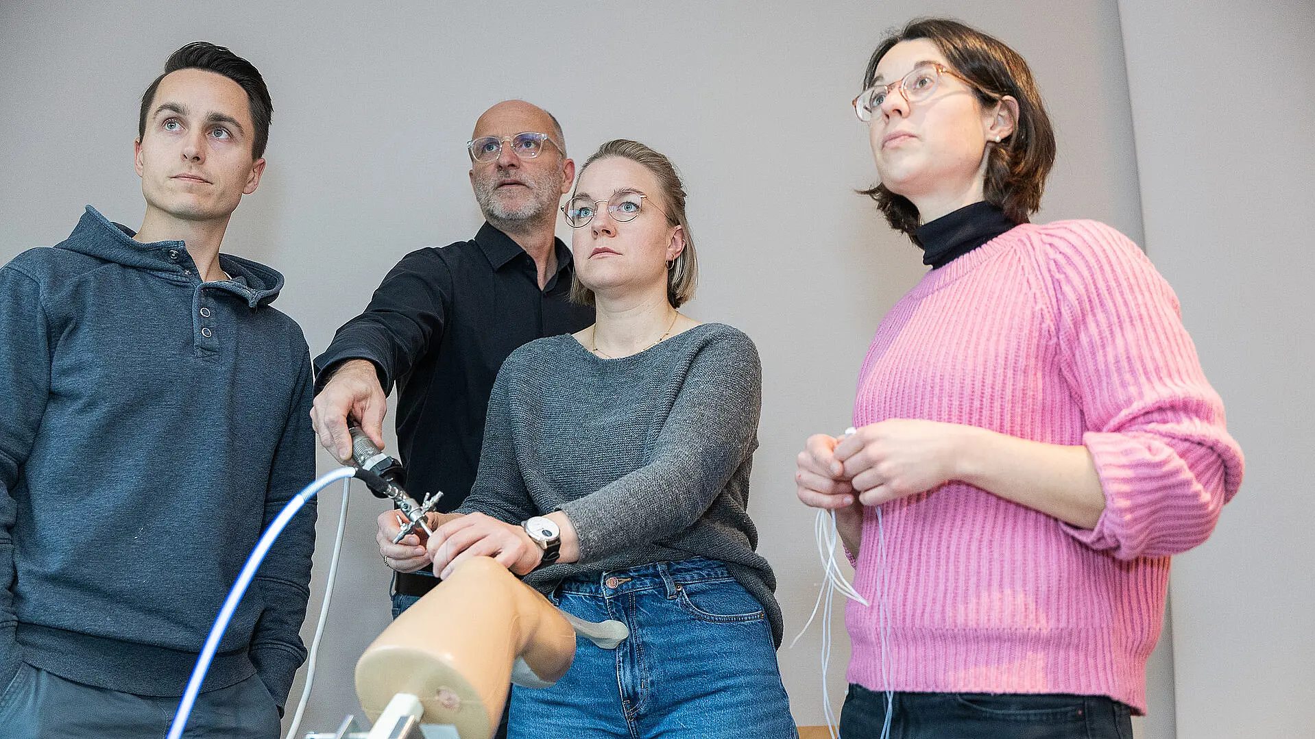 Vier Personen stehen in einem Schulungsraum und arbeiten gemeinsam an einem Trainingsmodell für eine Kniearthroskopie; eine Person demonstriert einen Arbeitsschritt, die anderen beobachten aufmerksam.