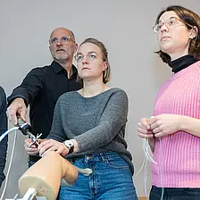 Vier Personen stehen in einem Schulungsraum und arbeiten gemeinsam an einem Trainingsmodell für eine Kniearthroskopie; eine Person demonstriert einen Arbeitsschritt, die anderen beobachten aufmerksam.