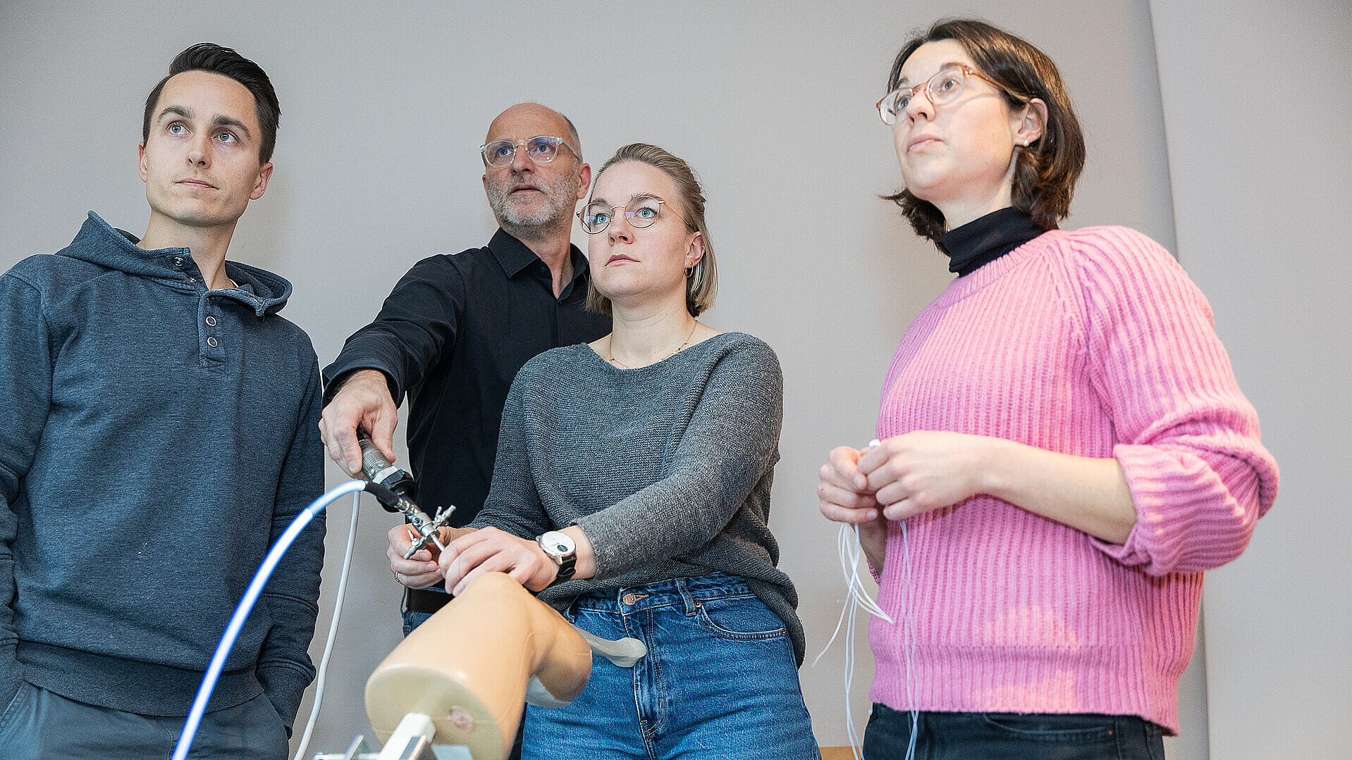 Vier Personen stehen in einem Schulungsraum und arbeiten gemeinsam an einem Trainingsmodell für eine Kniearthroskopie; eine Person demonstriert einen Arbeitsschritt, die anderen beobachten aufmerksam.