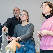 Vier Personen stehen in einem Schulungsraum und arbeiten gemeinsam an einem Trainingsmodell für eine Kniearthroskopie; eine Person demonstriert einen Arbeitsschritt, die anderen beobachten aufmerksam.