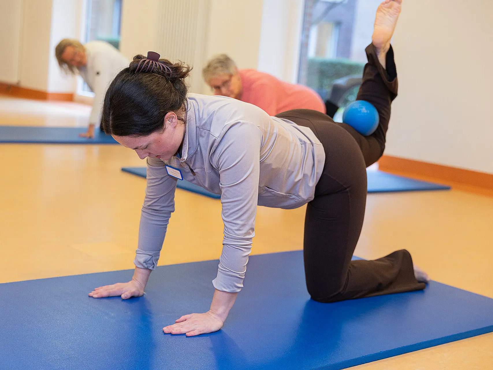 Eine Teilnehmerin macht eine Pilatesübung auf einer Matte mit einem Ball.