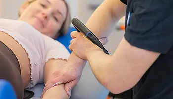 Ein Therapeut führt eine physikalische Therapie mit einem INDIBA-Gerät am Arm einer Patientin durch.