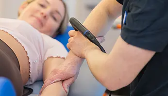 Ein Therapeut führt eine physikalische Therapie mit einem INDIBA-Gerät am Arm einer Patientin durch.