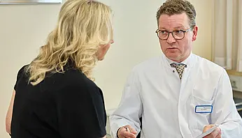 Dr. med. Ansgar Platte steht einer Patientin gegenüber und erläutert einen medizinischen Sachverhalt in ruhiger Gesprächssituation.