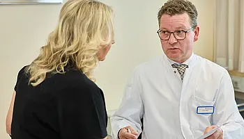 Dr. med. Ansgar Platte steht einer Patientin gegenüber und erläutert einen medizinischen Sachverhalt in ruhiger Gesprächssituation.