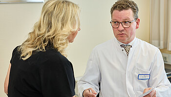 Dr. med. Ansgar Platte steht einer Patientin gegenüber und erläutert einen medizinischen Sachverhalt in ruhiger Gesprächssituation.