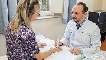 PD Dr. med. Peter Korsten untersucht die Hand einer sitzenden Patientin in einem Patientenzimmer.