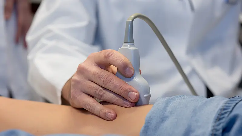 Die Hand von Dr. PD Daniel Windschall hält einen Ultraschallkopf auf dem Bauch eines liegenden Kindes während einer Untersuchung.