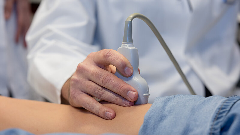 Die Hand von Dr. PD Daniel Windschall hält einen Ultraschallkopf auf dem Bauch eines liegenden Kindes während einer Untersuchung.