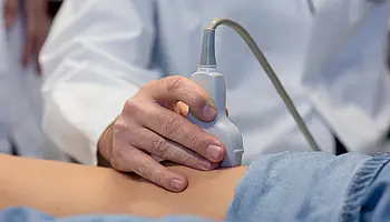 Dr. PD Daniel Windschall führt eine Ultraschalluntersuchung am Bein eines Kindes durch. Das Kind liegt entspannt auf einer Untersuchungsliege.