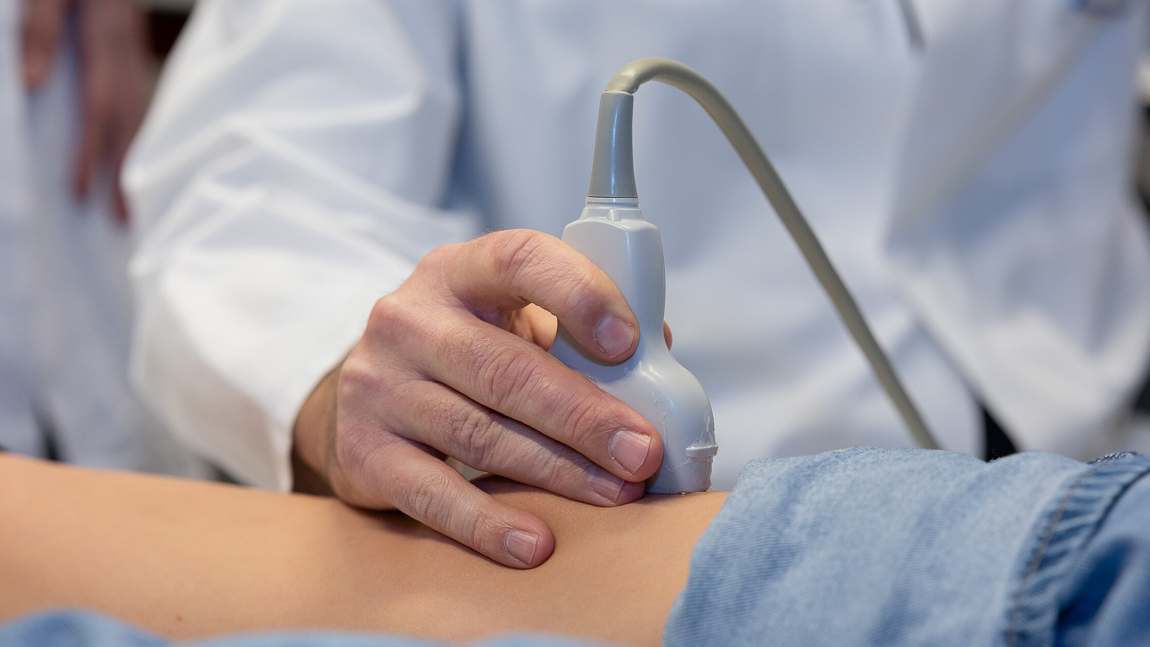 Ein Ultraschallkopf wird mit Kontaktgel auf ein Gelenk eines Kindes aufgesetzt und gehalten.