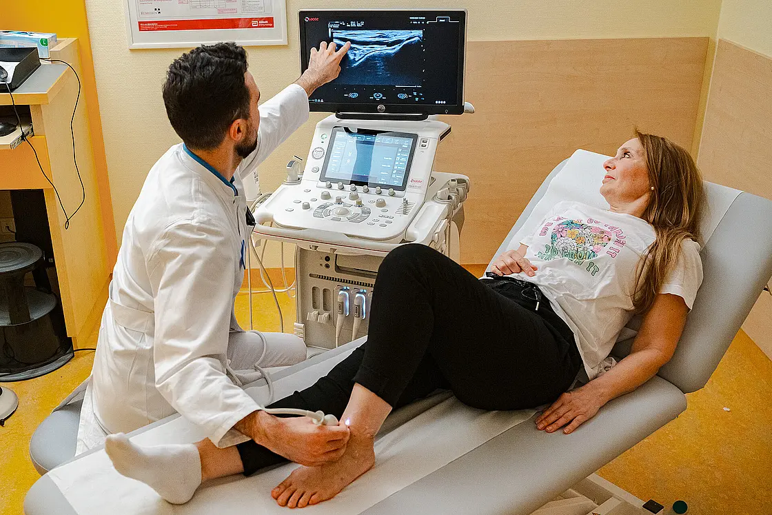 Behandelnde Person deutet auf den Ultraschallmonitor, während eine Patientin auf der Untersuchungsliege liegt.