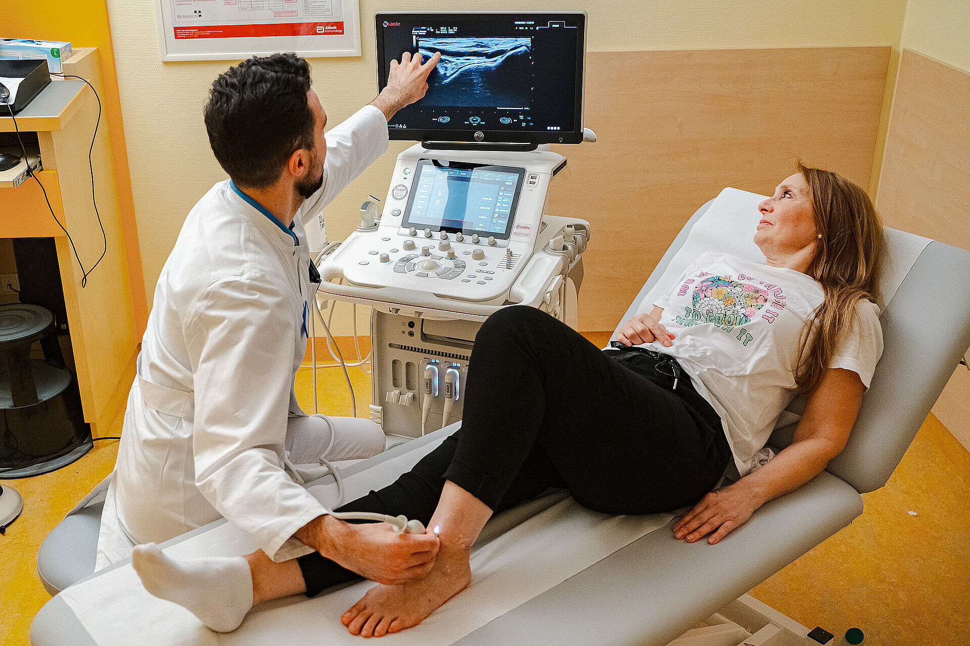 Behandelnde Person deutet auf den Ultraschallmonitor, während eine Patientin auf der Untersuchungsliege liegt.