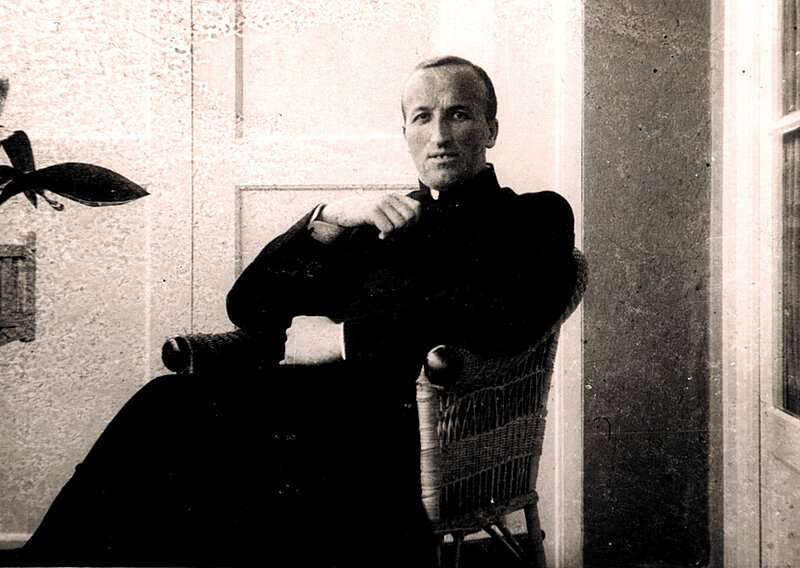 Historisches Schwarzweißporträt eines sitzenden Mannes in dunkler Kleidung vor schlichtem Hintergrund.