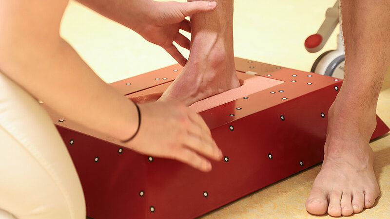 Ein Fuß steht in einer roten Messbox, während eine Fachkraft die Position mit den Händen kontrolliert.