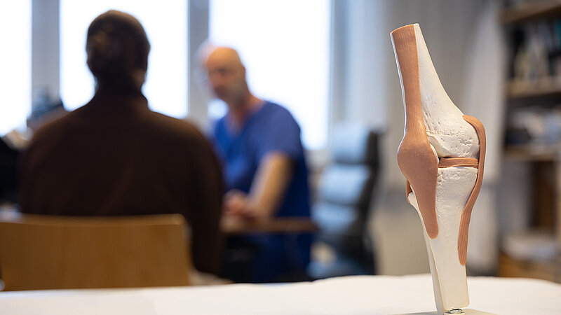 Kniemodell im Vordergrund, Arztgespräch im Hintergrund