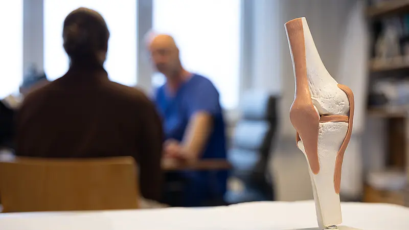 Kniemodell im Vordergrund, Arztgespräch im Hintergrund