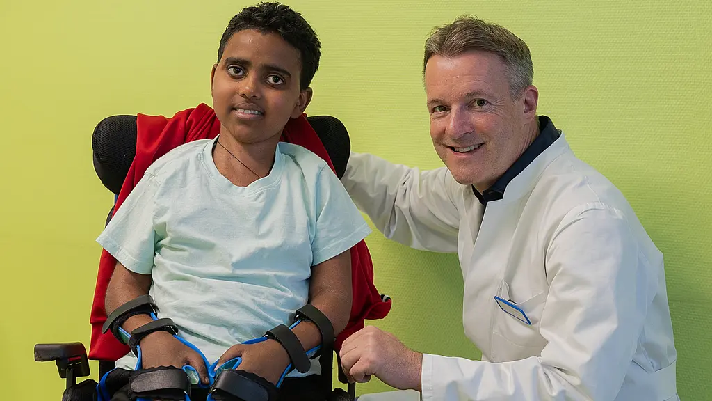 Siyum Siem aus Eritrea hat eine seltene Erkrankung, die von den Symptomen her Rheuma ähnelt. Seine Mutter begleitete ihn in die Klinik für Kinder- und Jugendrheumatologie, wo er von Chefarzt PD Dr. Daniel Windschall und seinem Team behandelt wurde. Ein eritreischer Junge in einem Rollstuhl neben seinem behandelnden Arzt.