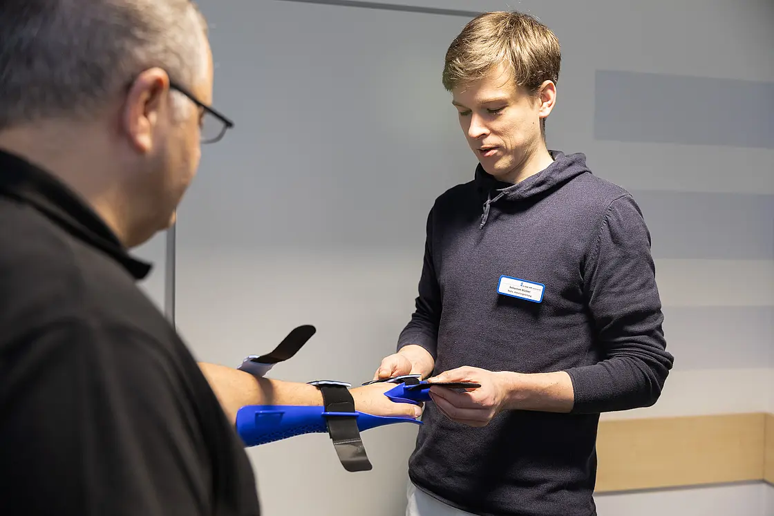 Ein Orthopädietechnikmechaniker passt einem Patienten am ausgestreckten Arm eine Handorthese an.