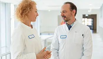 PD Dr. med. Peter Korsten steht in einem Klinikflur und spricht mit Dr. Anna Maier.