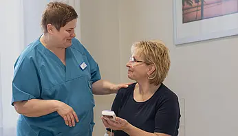 Eine Pflegefachperson erklärt einer Patientin die Anwendung eines TENS-Geräts und legt dabei beruhigend die Hand auf ihre Schulter.