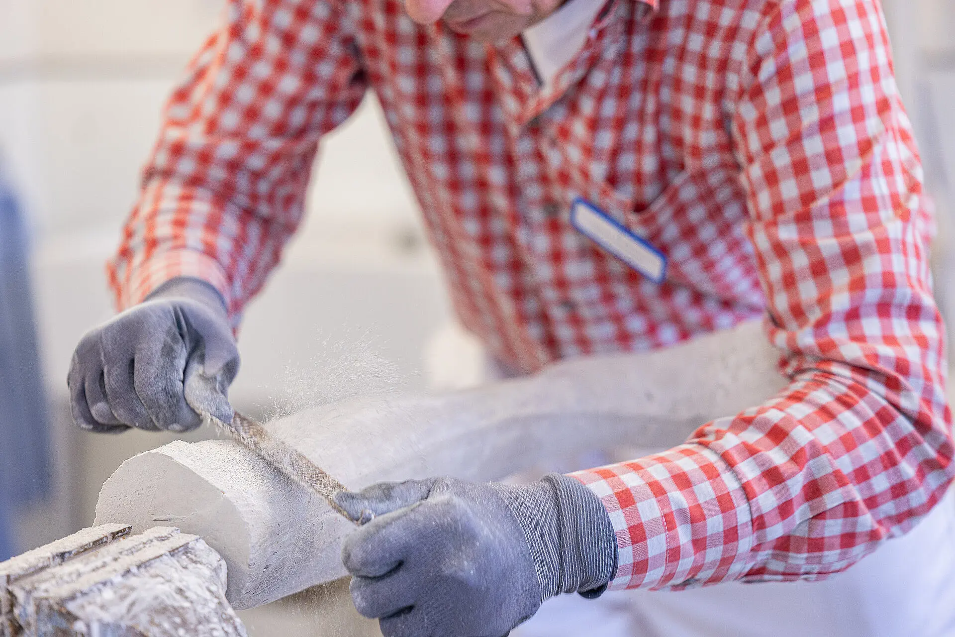 Mitarbeiter steht an einer Werkbank und formt ein Gipsleistenmodell mit einer Handraspel.